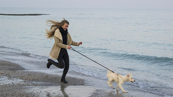 lady running down the beach with a dog